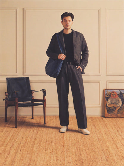 Man in a stylish outfit standing in a room with a chair and painting.